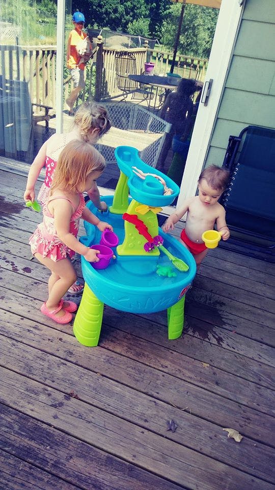 Three children playing with a water table on a deck