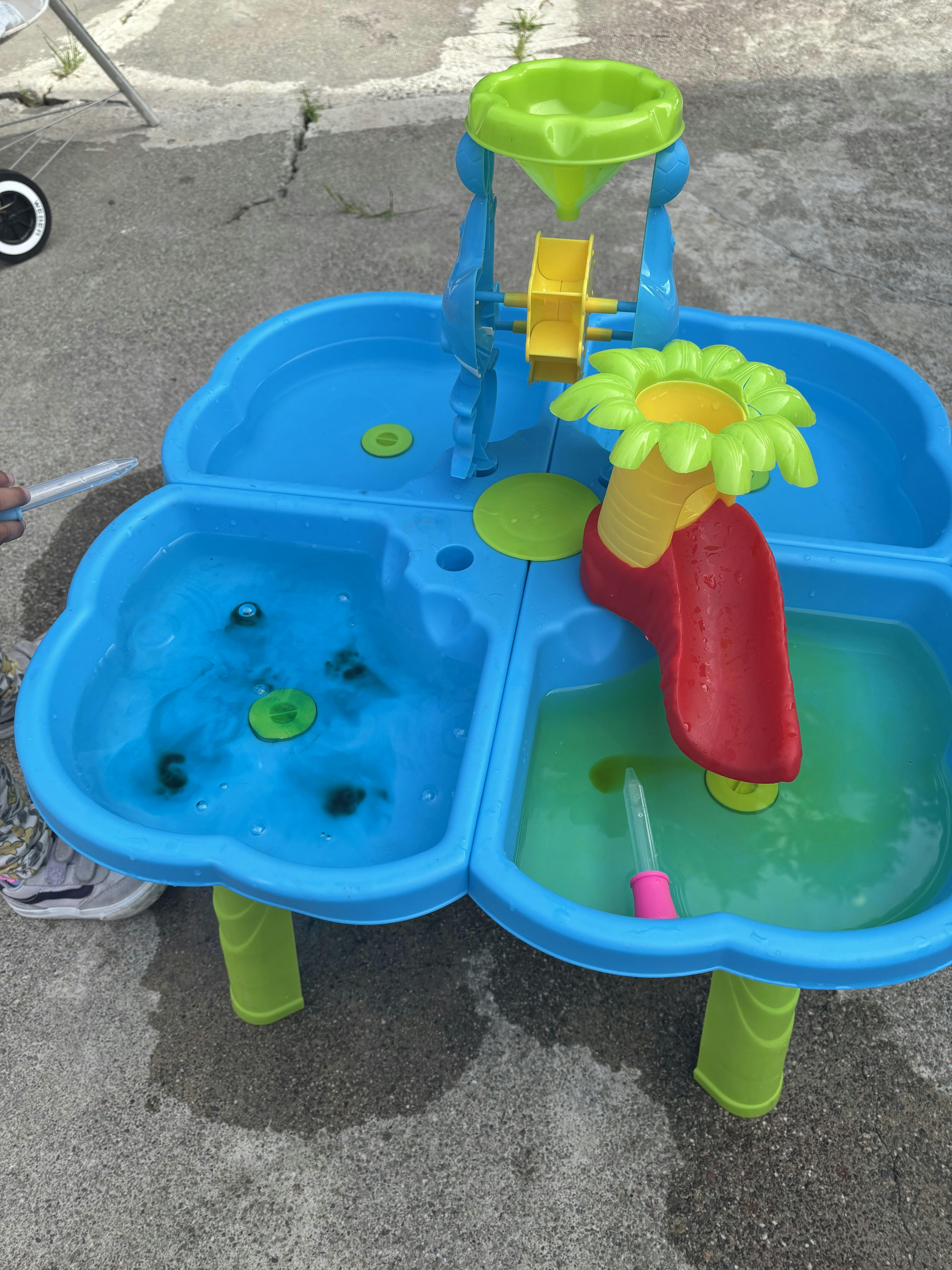 Child's hand holding a dropper over a blue water table with colorful toys