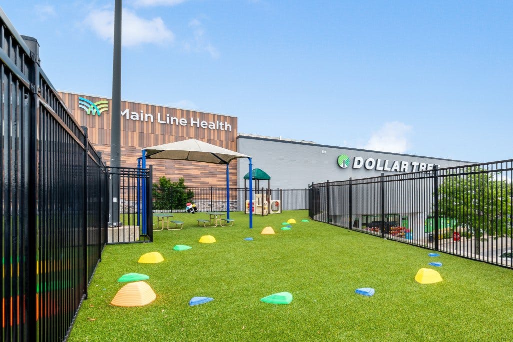 Playground with turf, small climbing structure, shade canopy, and picnic tables