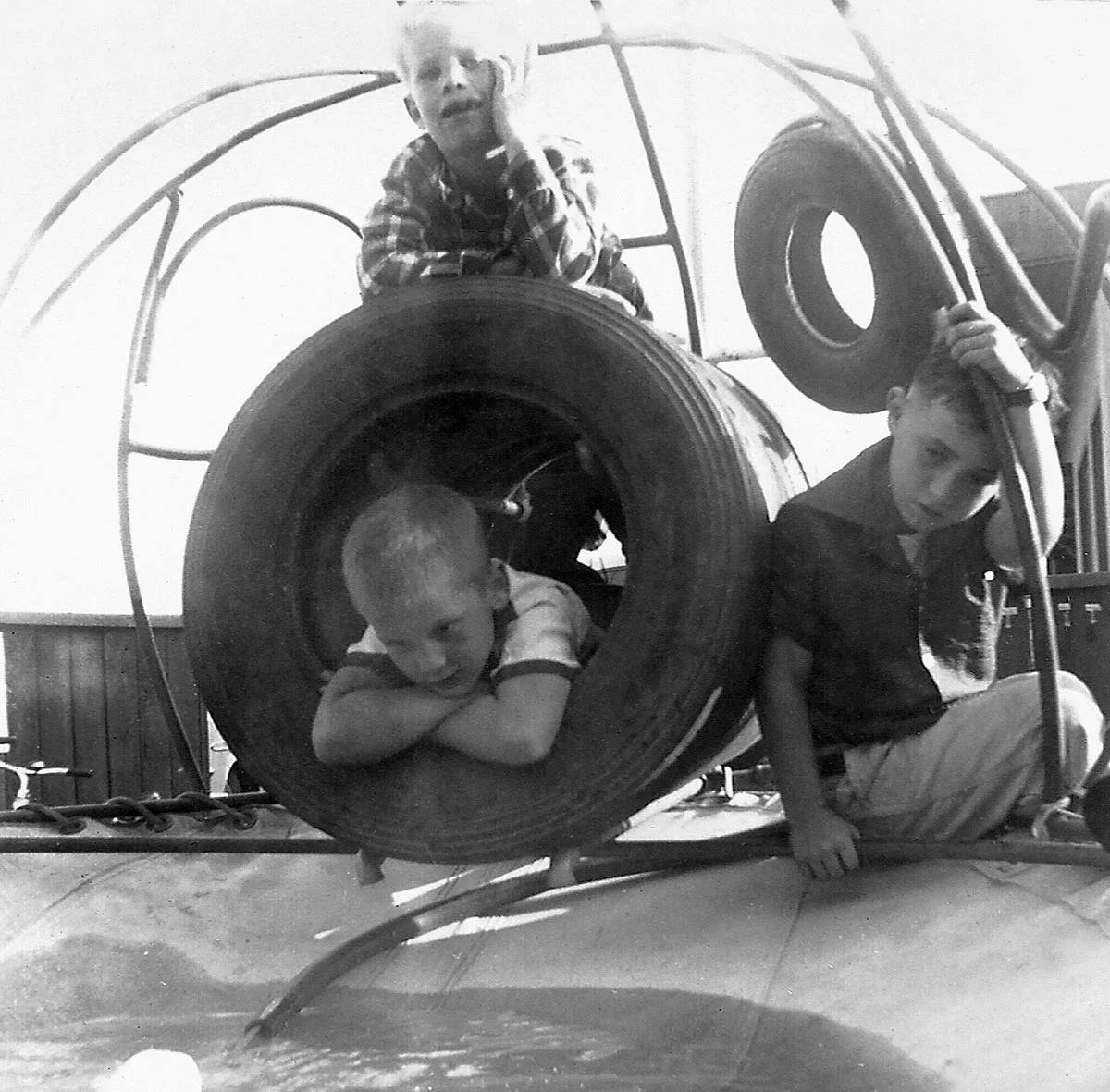 Three children playing on tires and a structure, one peeking from a tire