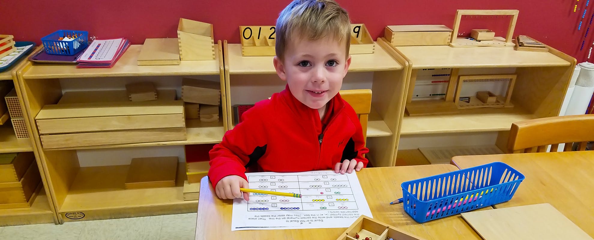 Child in a classroom holding a pencil over a worksheet