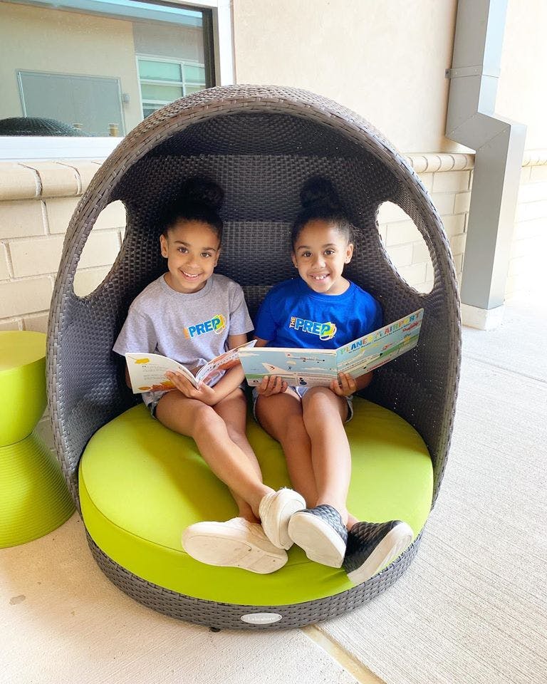 Two children sitting in a chair reading books