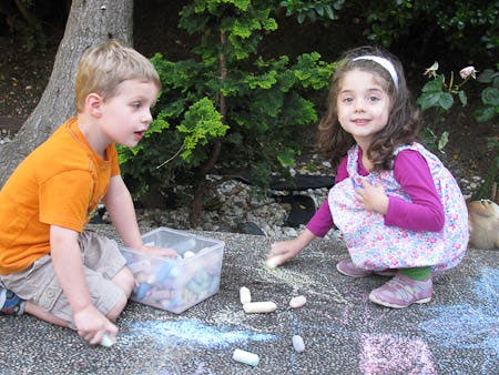 Two children drawing with chalk on pavement
