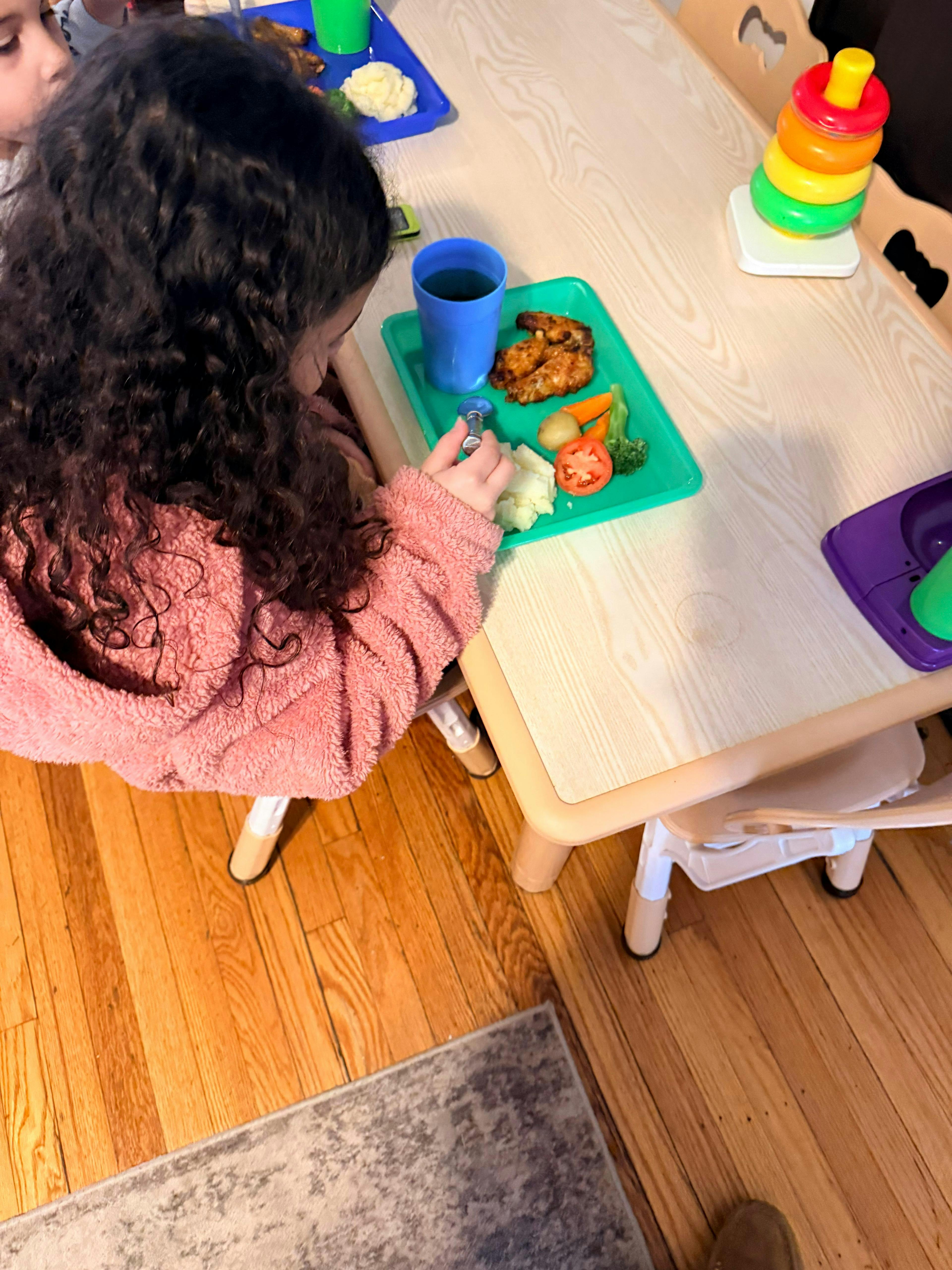 Child eating a meal on a green tray at a table