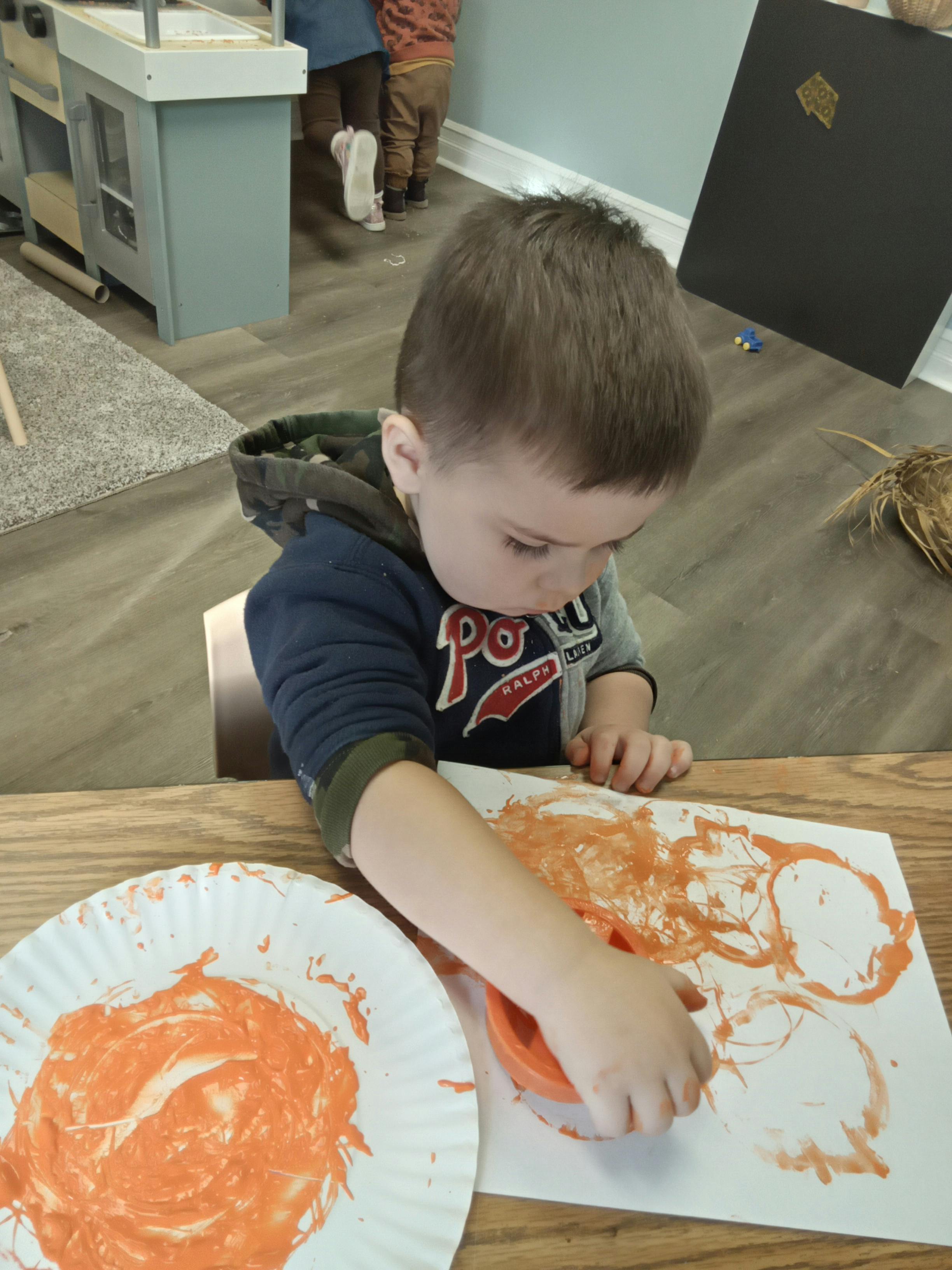 Child painting on paper with an orange paint-dipped container