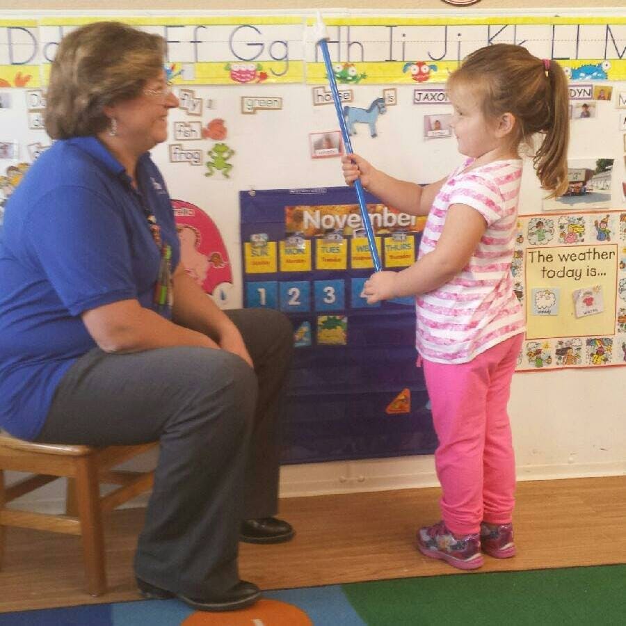 Adult and child in a classroom, child holding a pointer stick