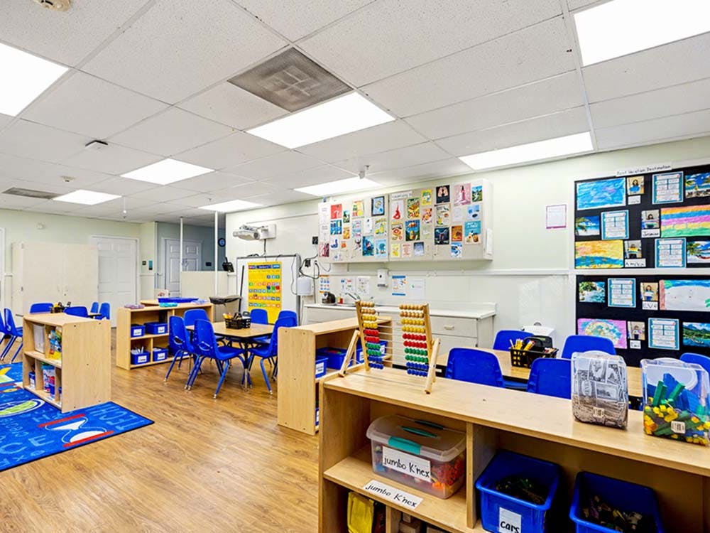 Empty classroom with small tables, blue chairs, and children's artwork on the walls