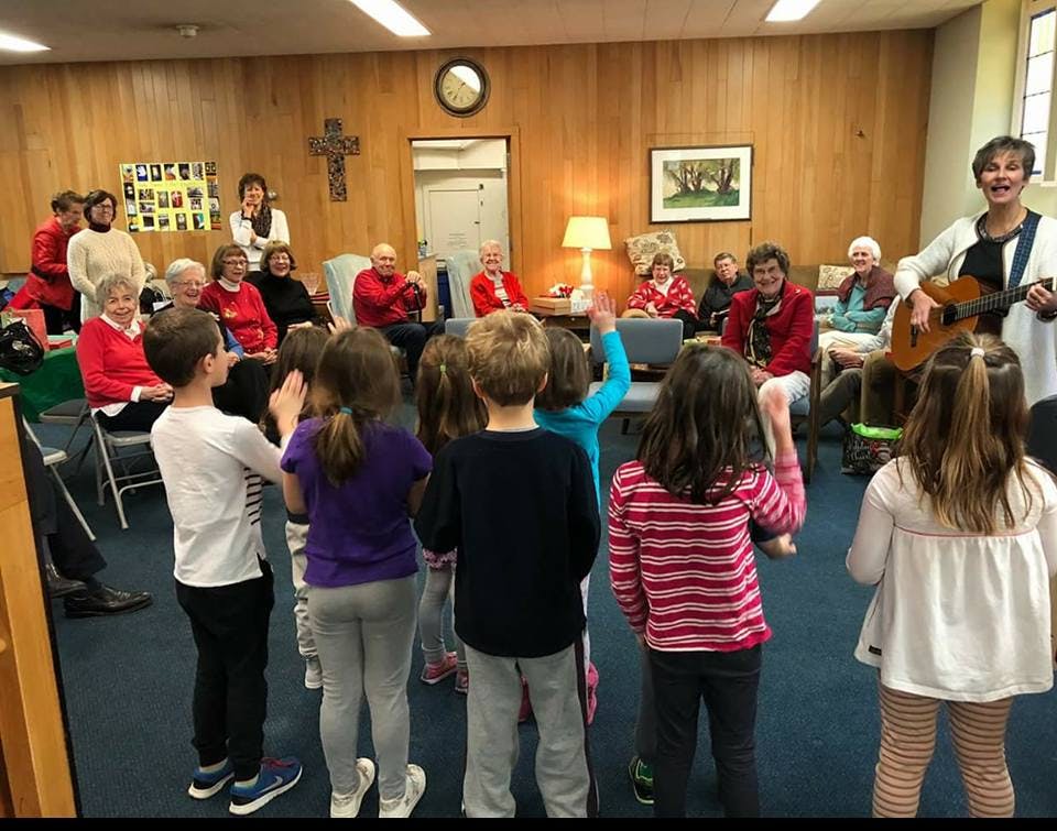 Adults and children gathered, person playing guitar