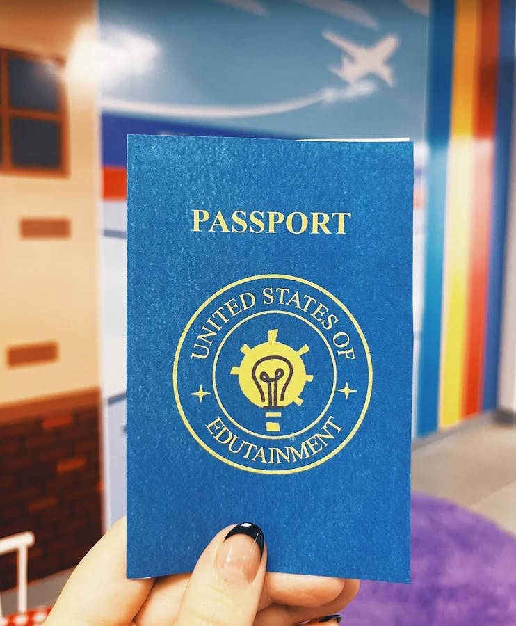 Hand holding a blue passport with "United States of Edutainment" seal