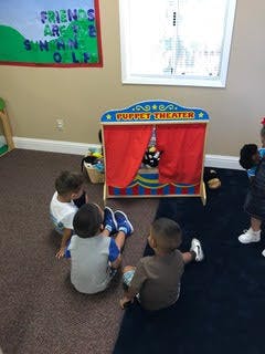 Three children sitting on the floor in front of a puppet theater