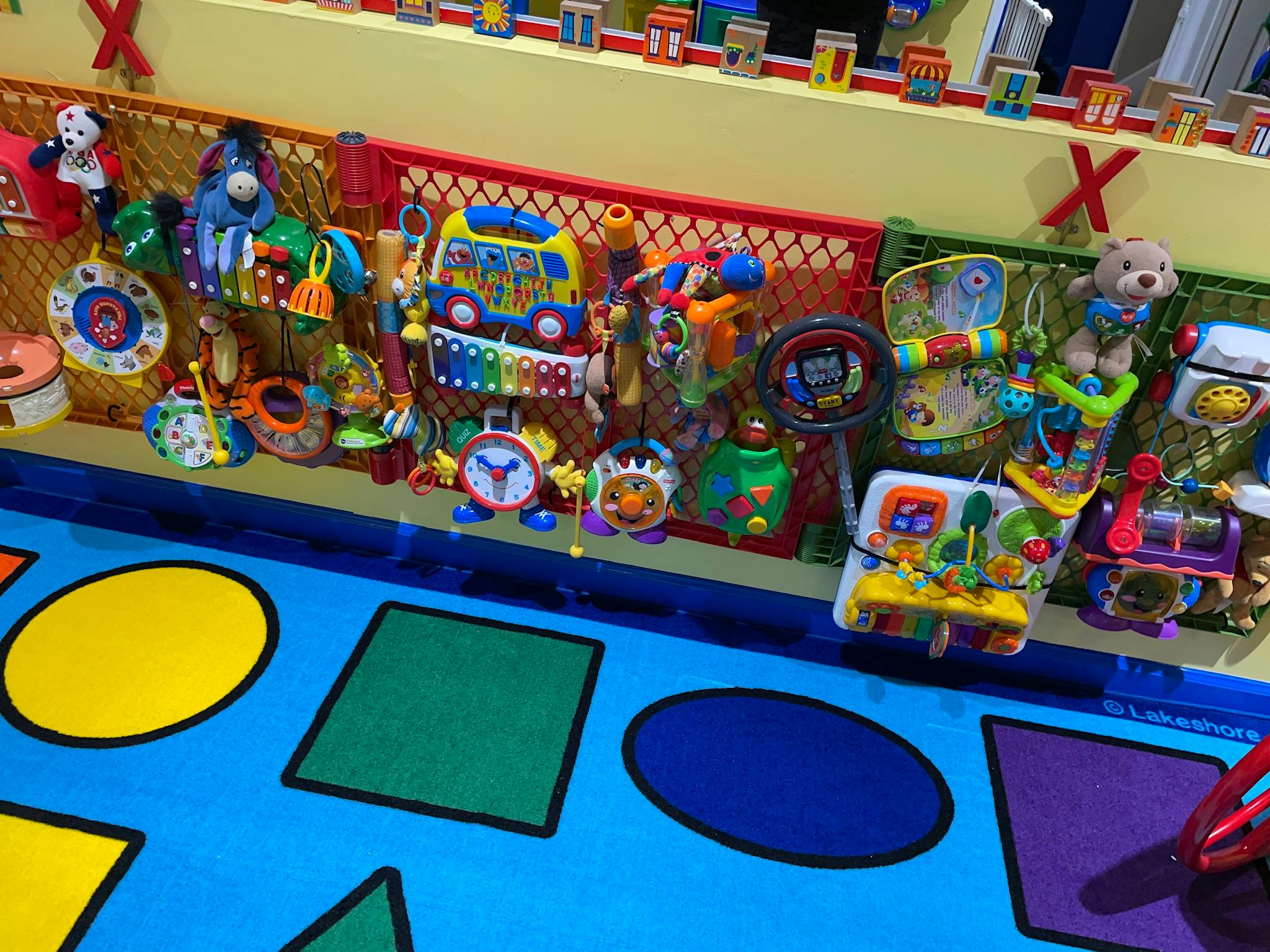 Children's toys on a shelf above a rug with colorful shapes