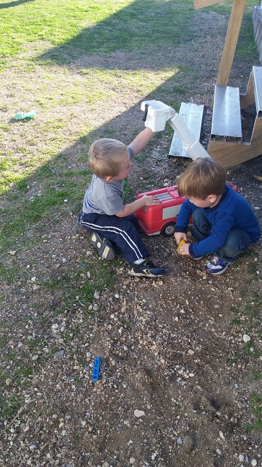 Two children playing with toys on a dirt and grass surface