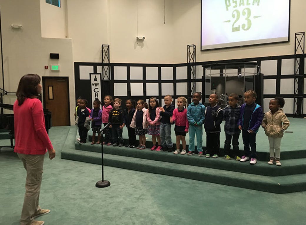 Person facing a line of children on a stage
