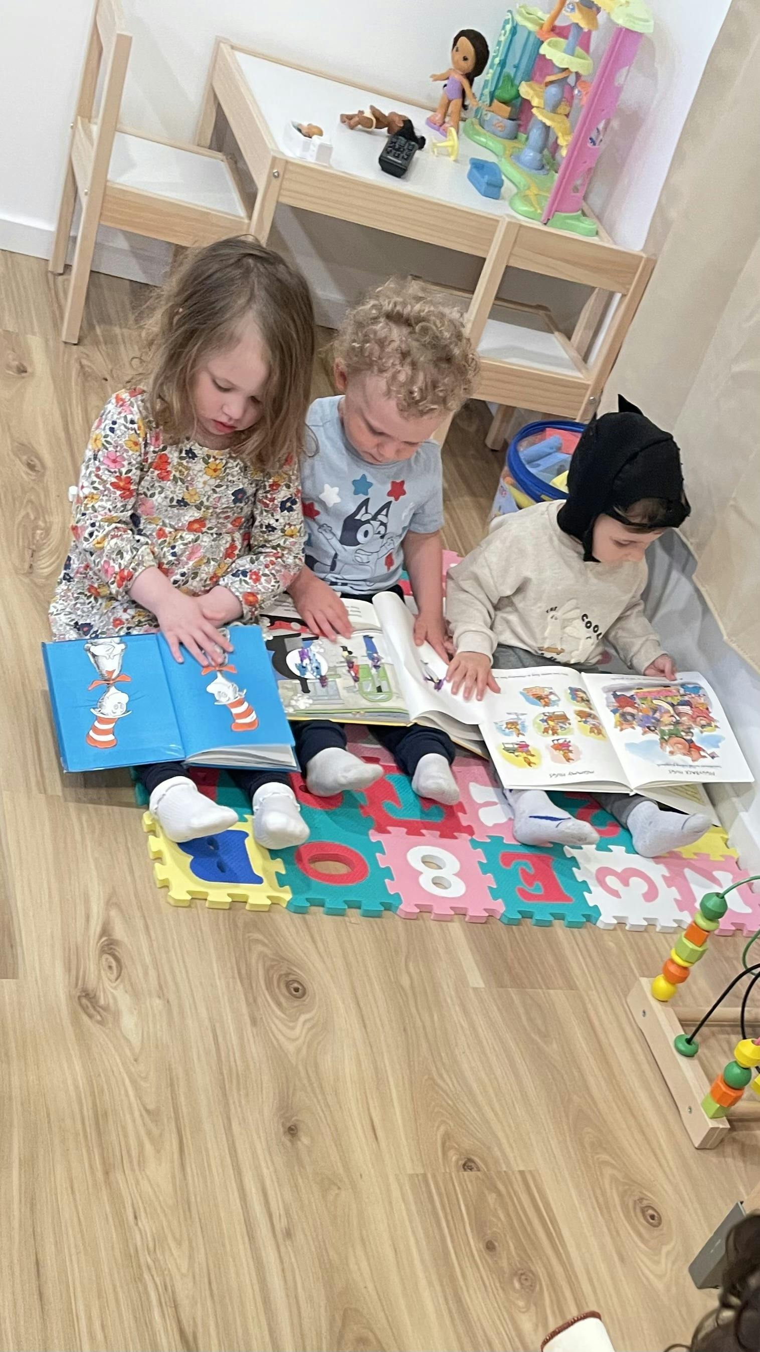 Three children sitting on a playmat, each reading a book