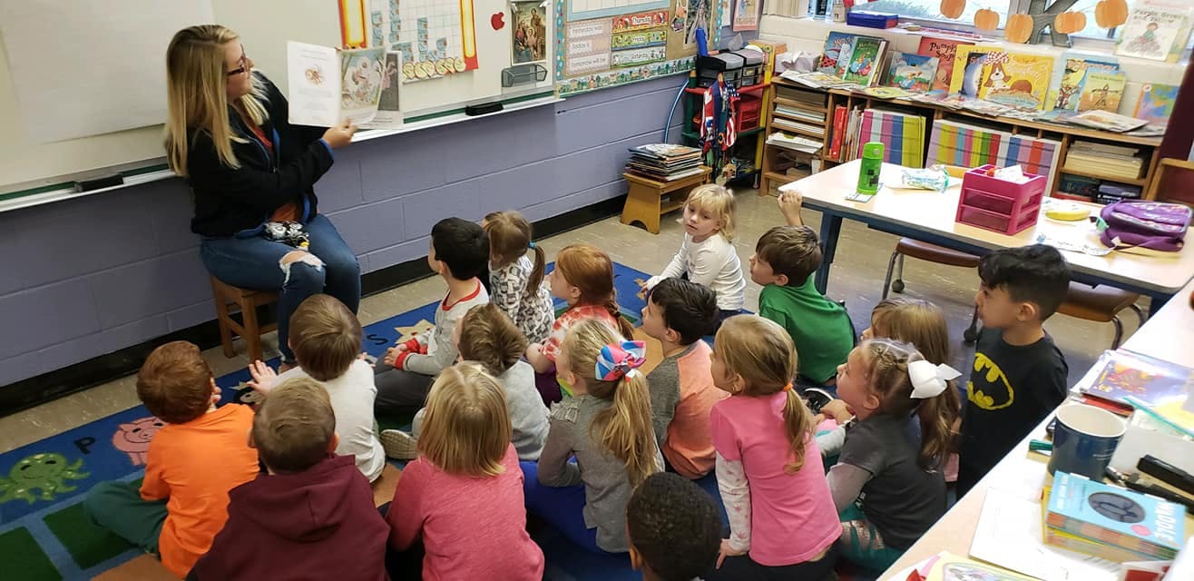 Person reading a book to children in a classroom