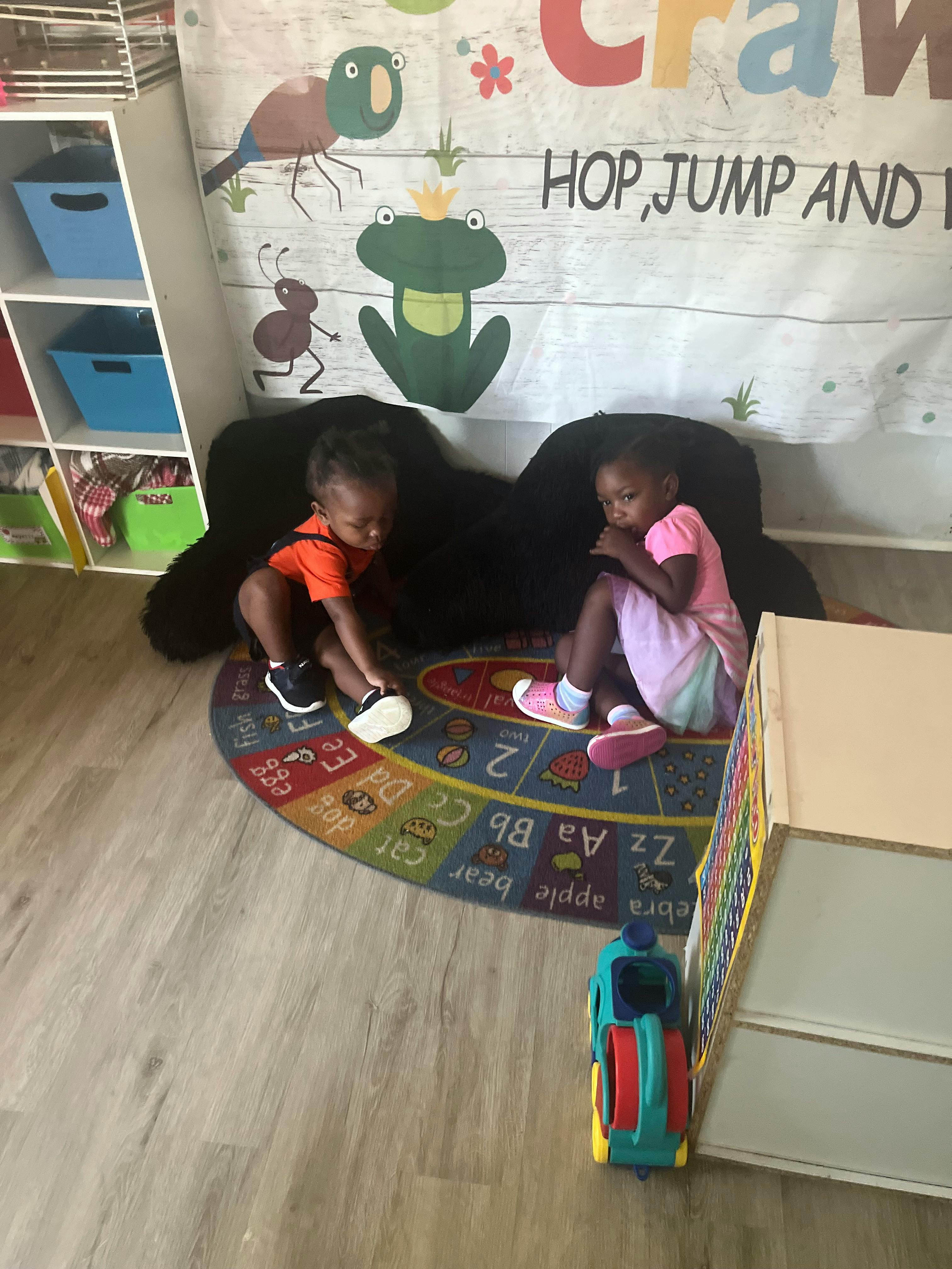 Two children sitting on a rug with alphabet letters