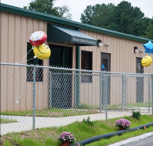Building with "Dream World Academy" sign and balloons behind a chain link fence
