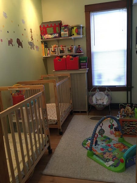 Three cribs in a room with a play mat and shelves of toys