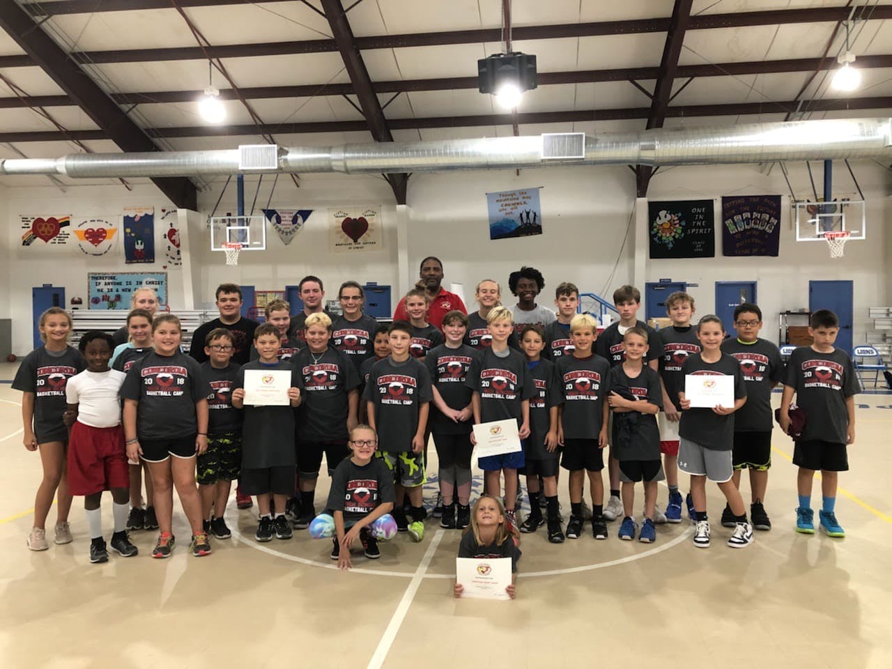 Group of children and adults posing with certificates in a gymnasium