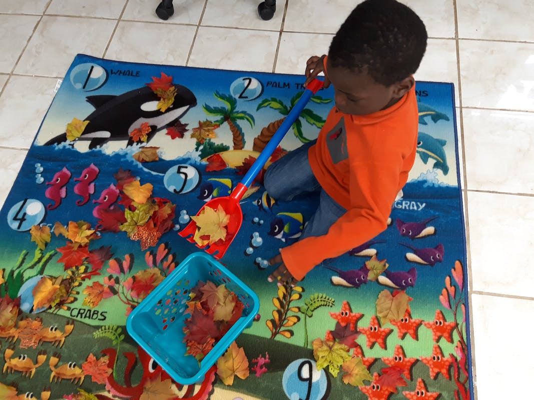 Child playing with leaves and a shovel on a colorful mat