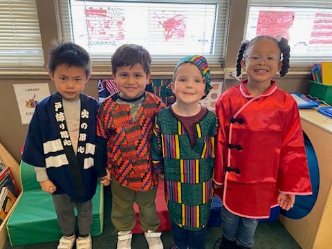 Four children in cultural clothing standing in a classroom