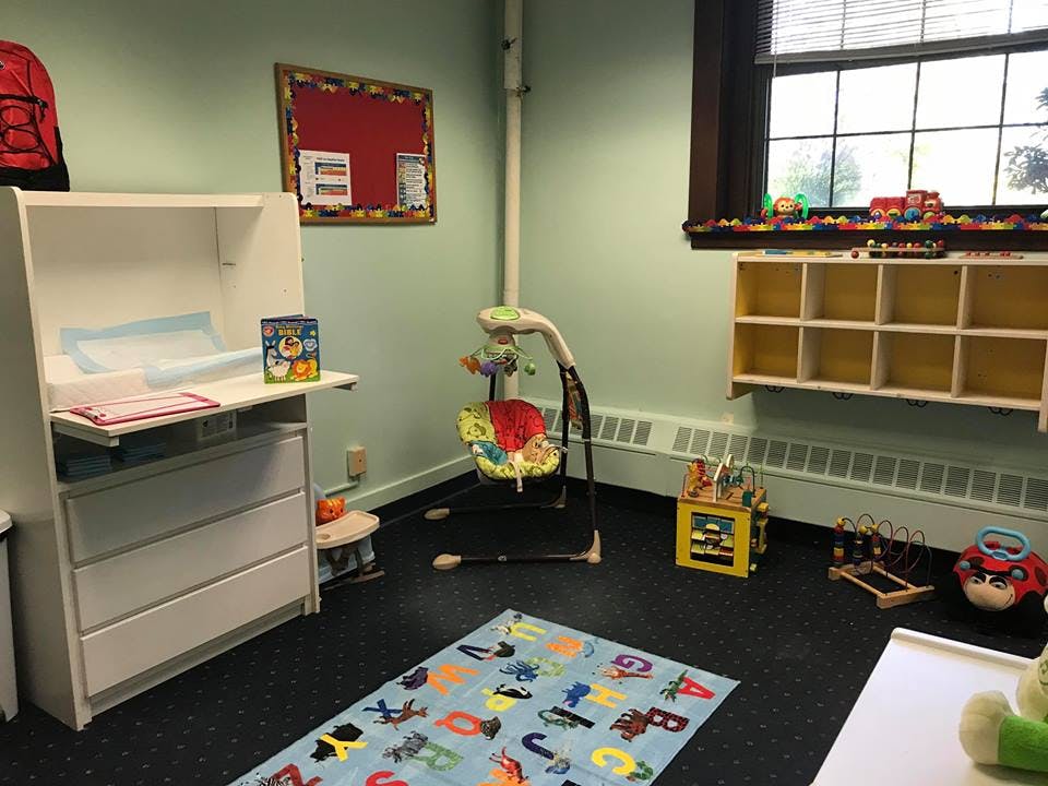 Nursery room with changing table, baby swing, and alphabet rug