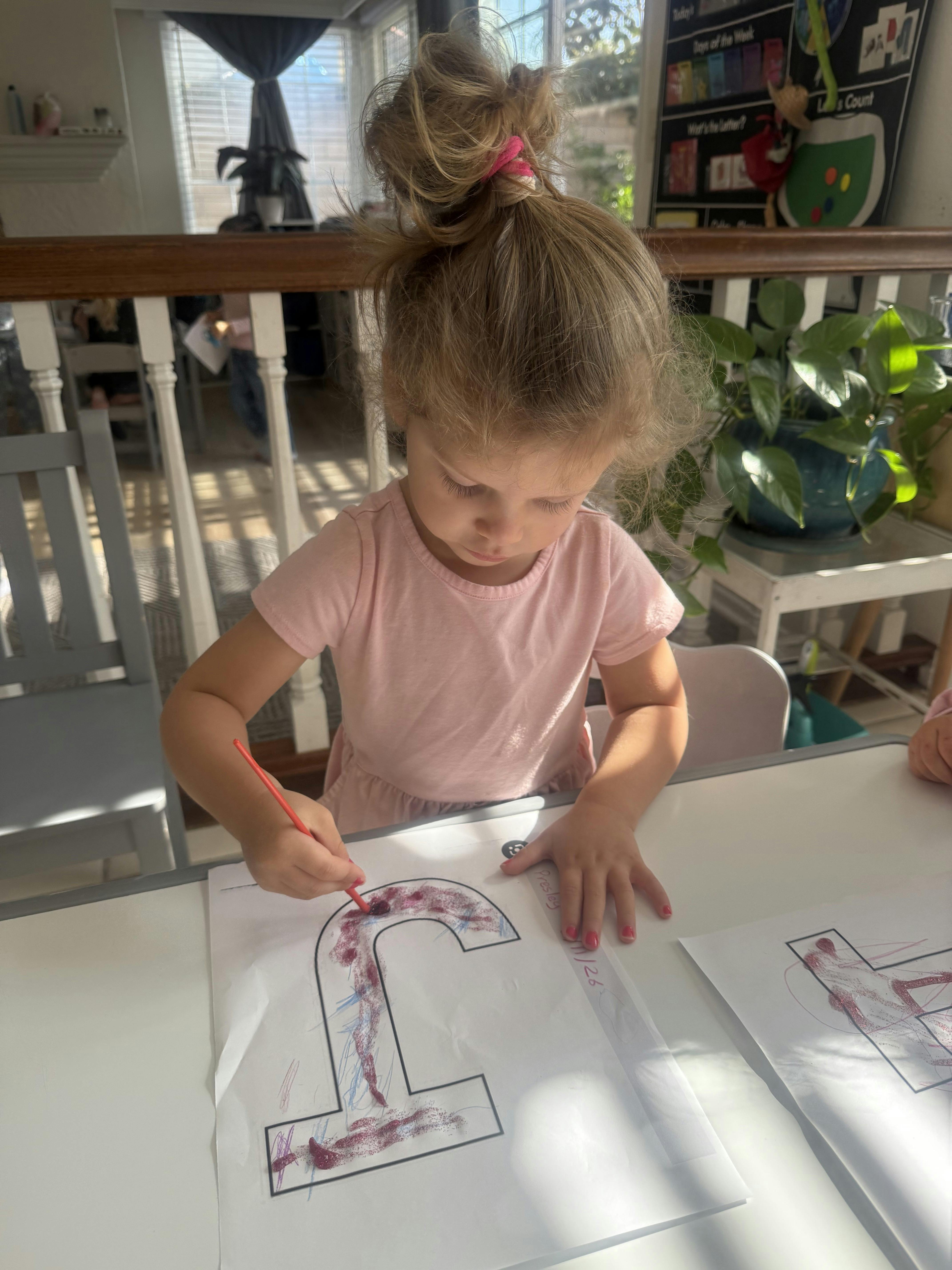 Child painting a large letter on a paper at a table