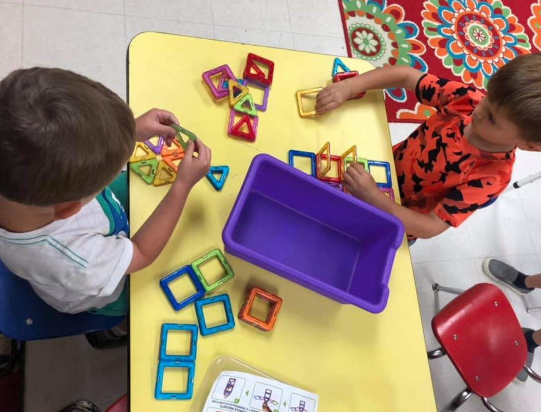 Two children playing with colorful magnetic building blocks at a table