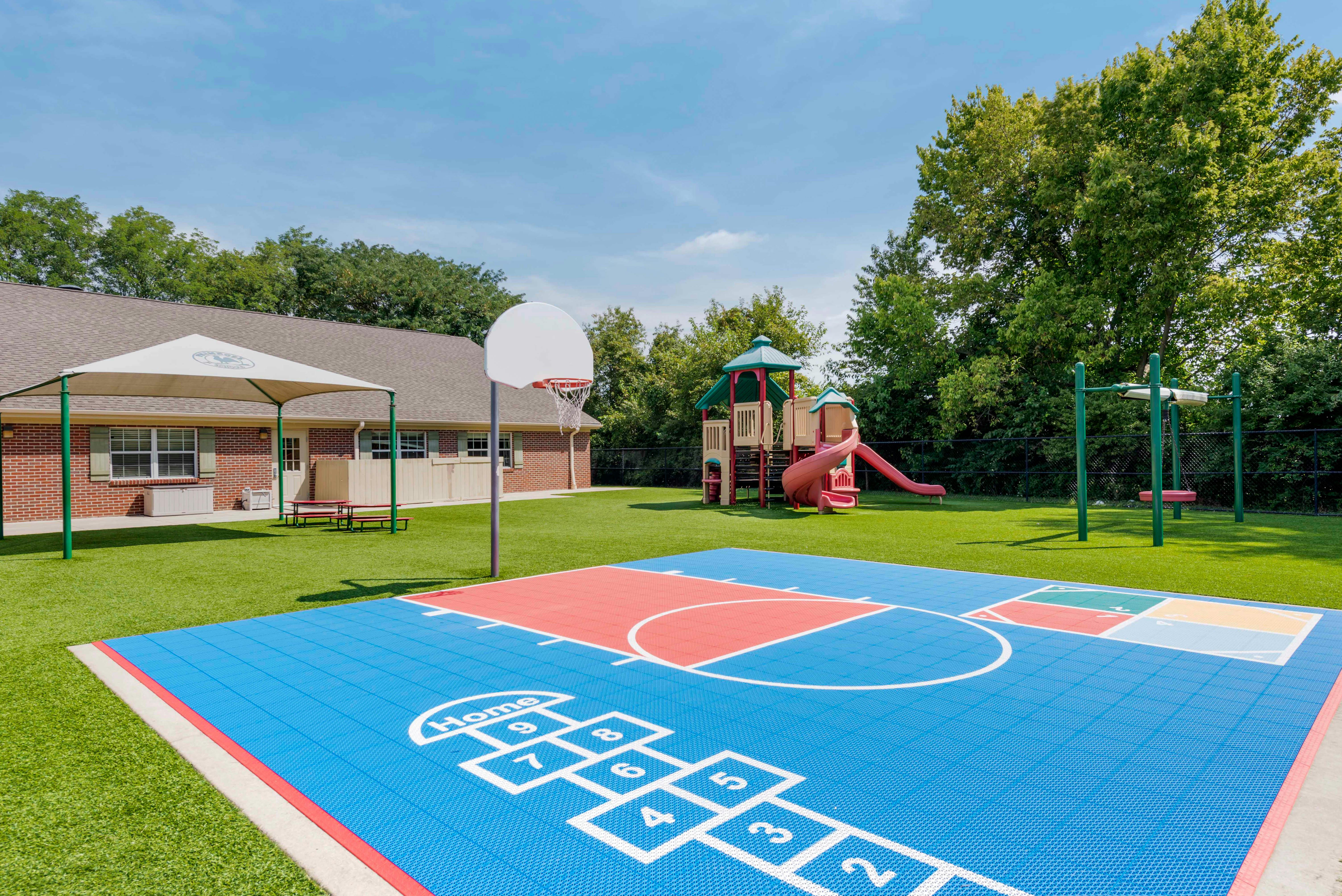Outdoor playground with a basketball court, play structure, and swing set