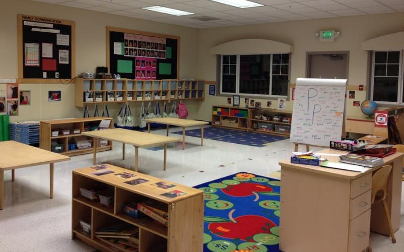 An empty classroom with small tables, chairs, cubbies, and a whiteboard with the letter P