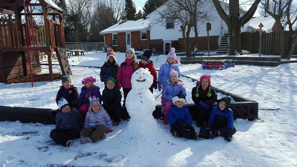 Group of children gathered around a snowman in a snowy playground