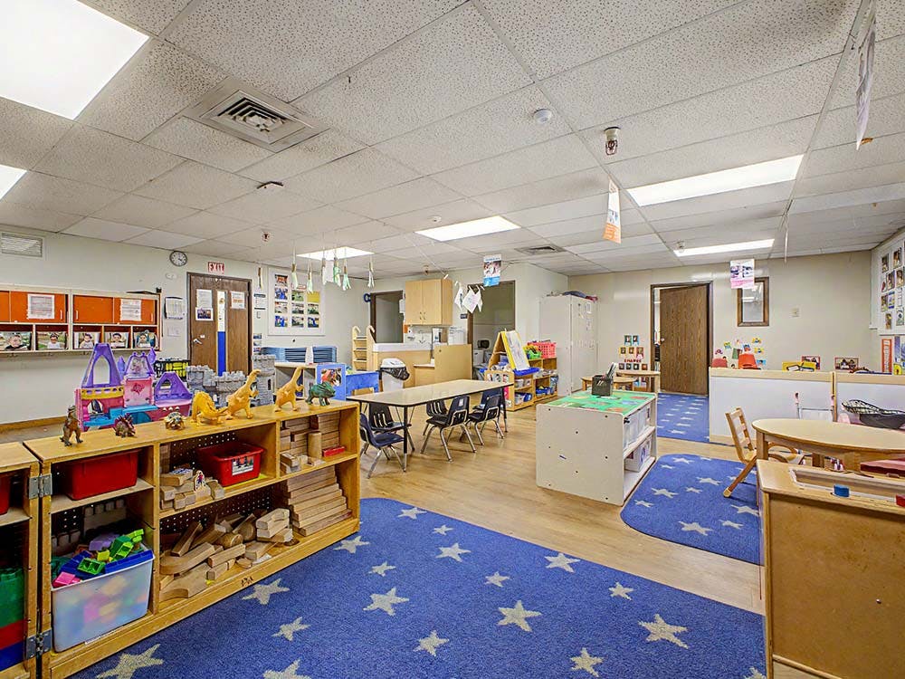 An empty children's classroom with blue star-patterned rugs and play areas