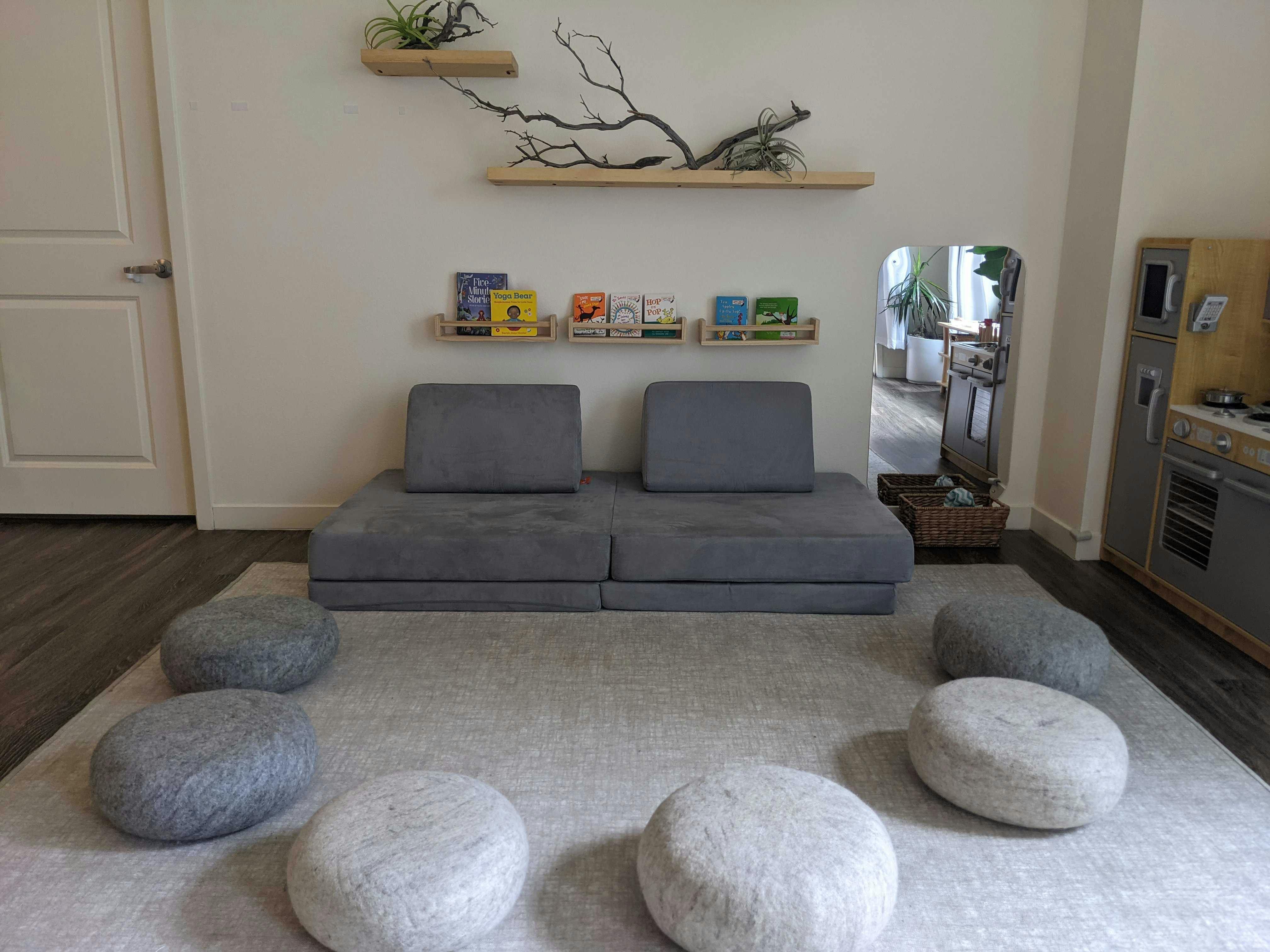 Living room with gray modular sofa, floor cushions, and wall shelves