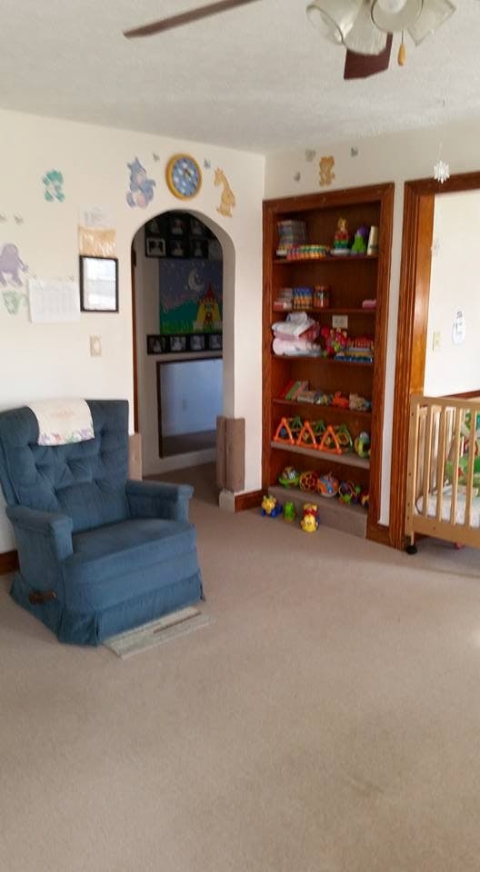 Nursery room with a blue armchair, bookshelf with toys, and a crib