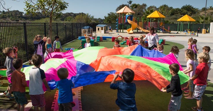 Children playing with a colorful parachute on a playground