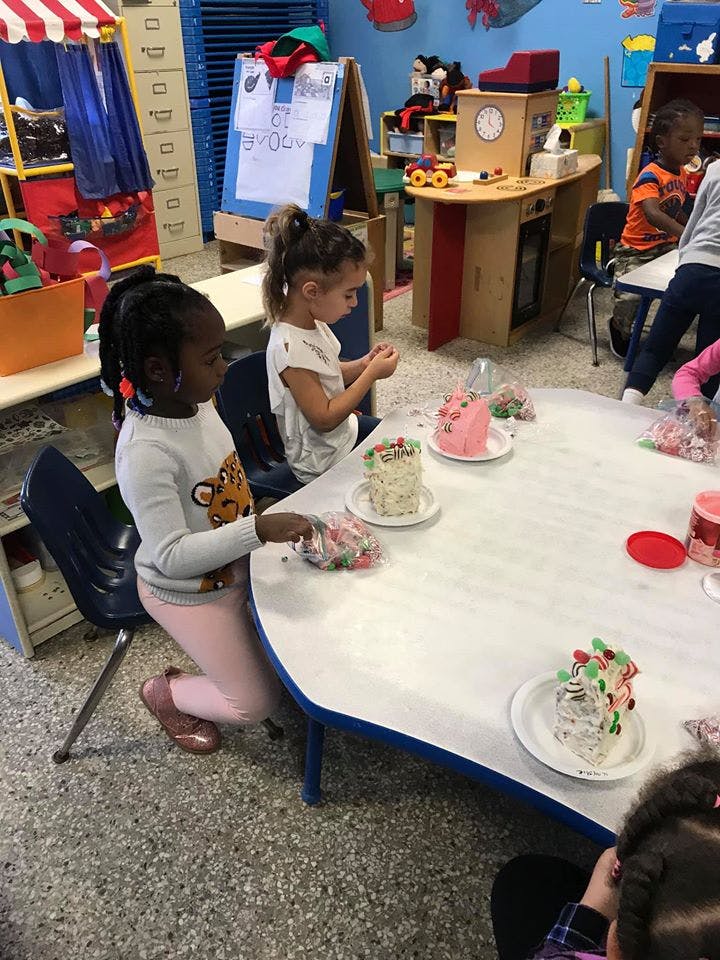 Two children decorating small cakes at a table in a classroom