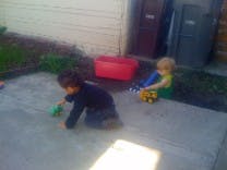 Two children playing with toys on a paved surface