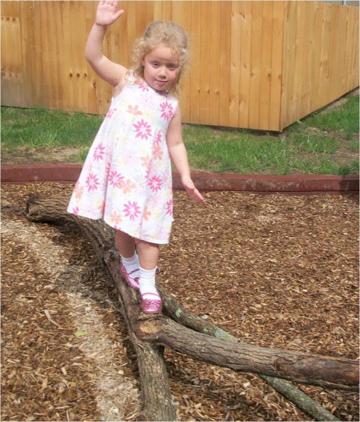 Child balancing on a log with arms raised