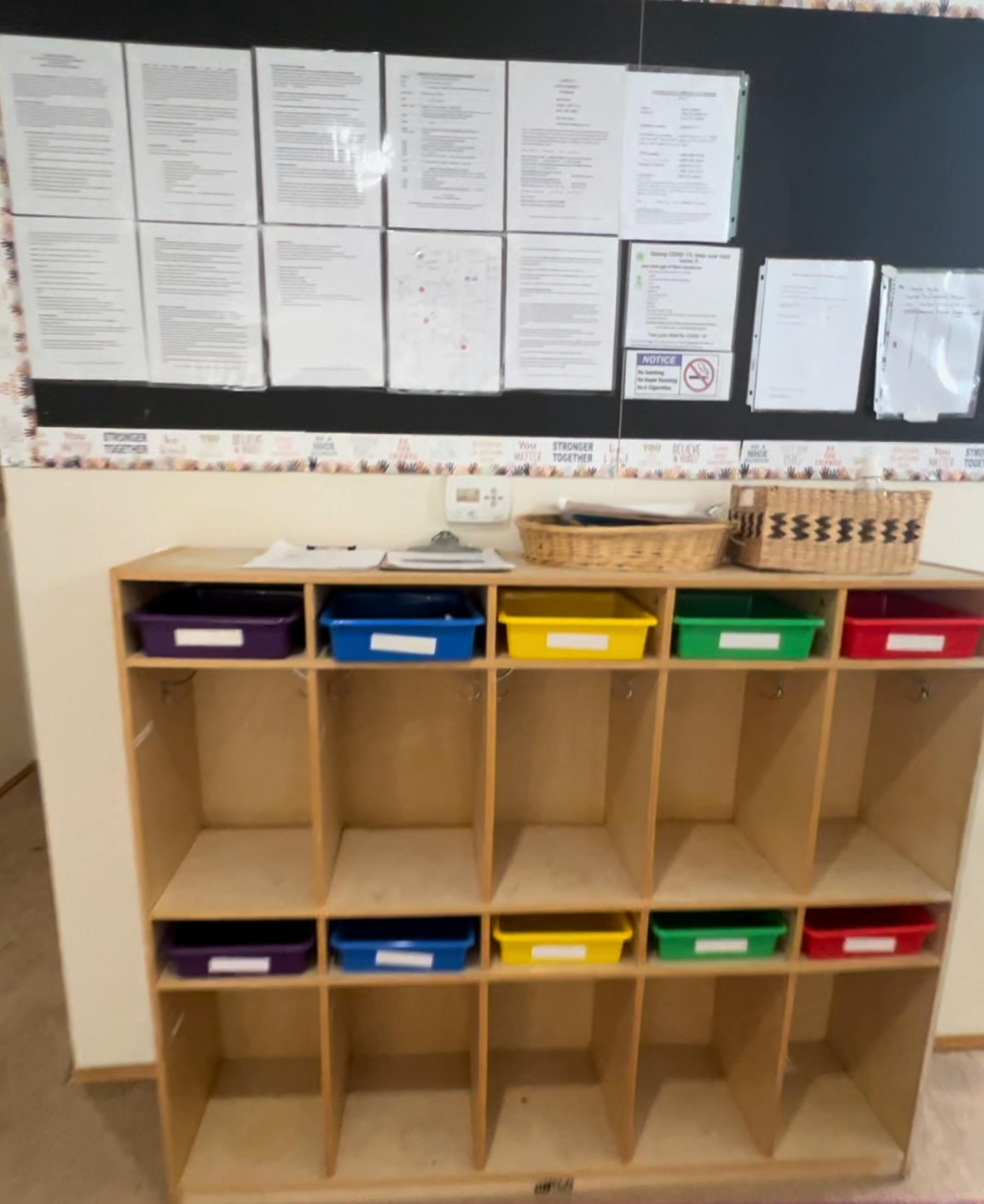 Wooden cubby shelf with colorful bins and papers on a bulletin board