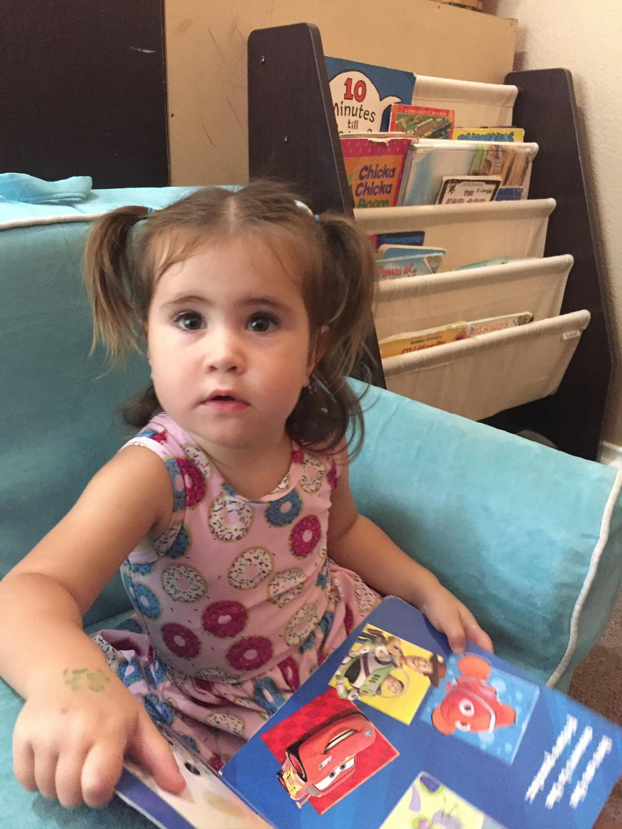 Child with pigtails sitting in a chair holding a book