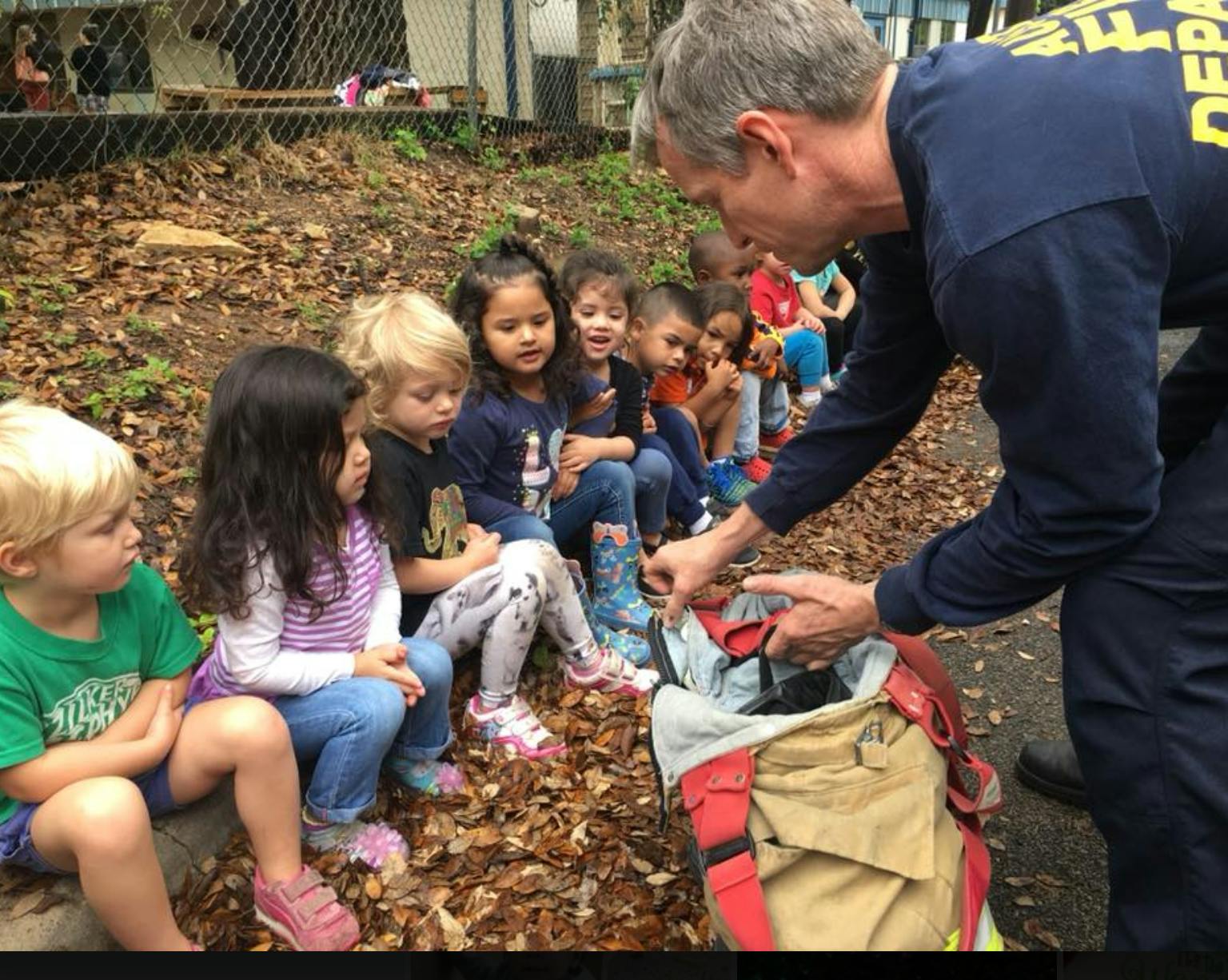 Adult showing items from a bag to a group of children sitting on the ground
