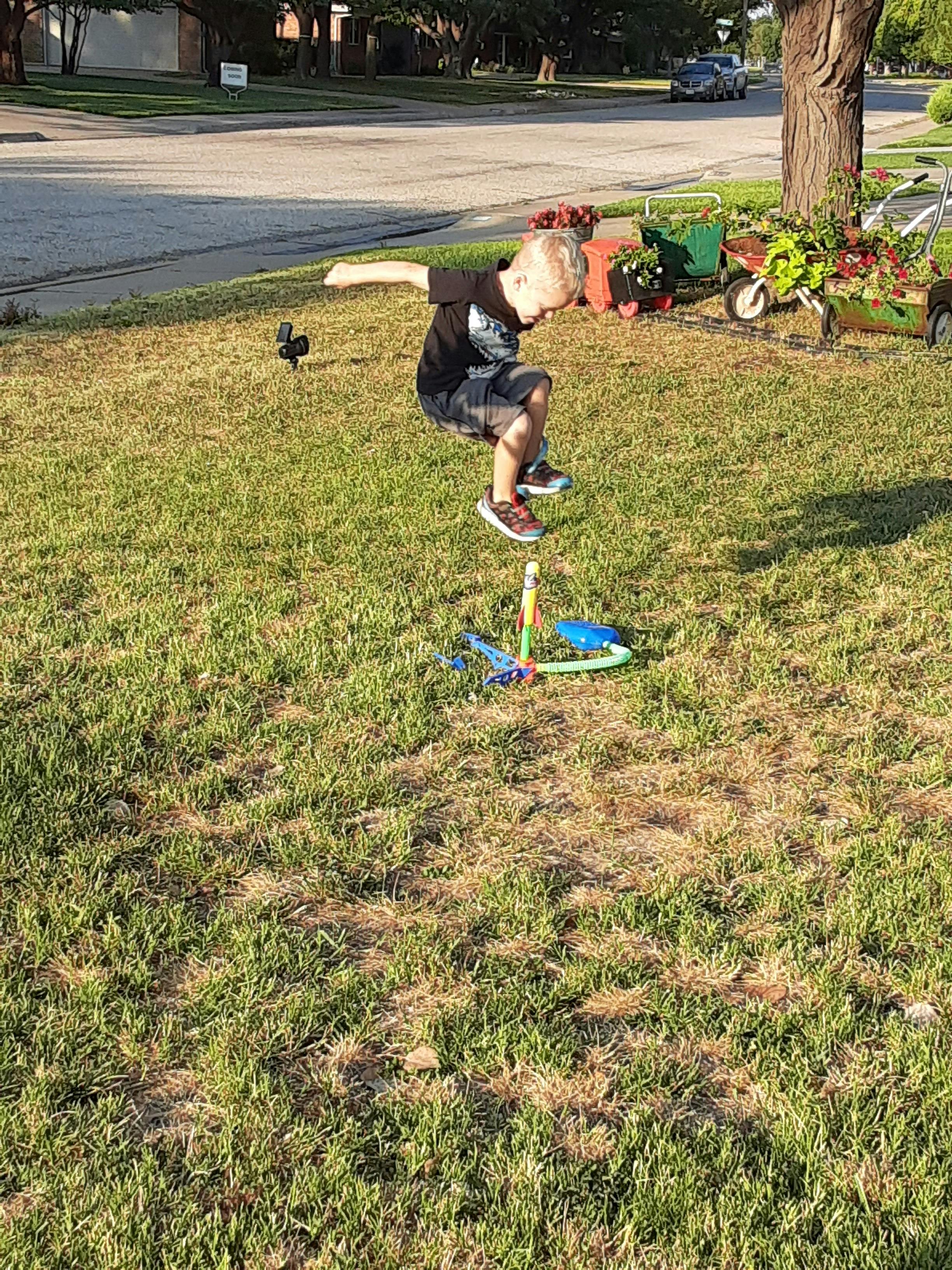 Child jumping on a toy rocket launcher in grass