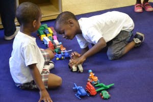 Two children playing with toy cars and blocks on the floor