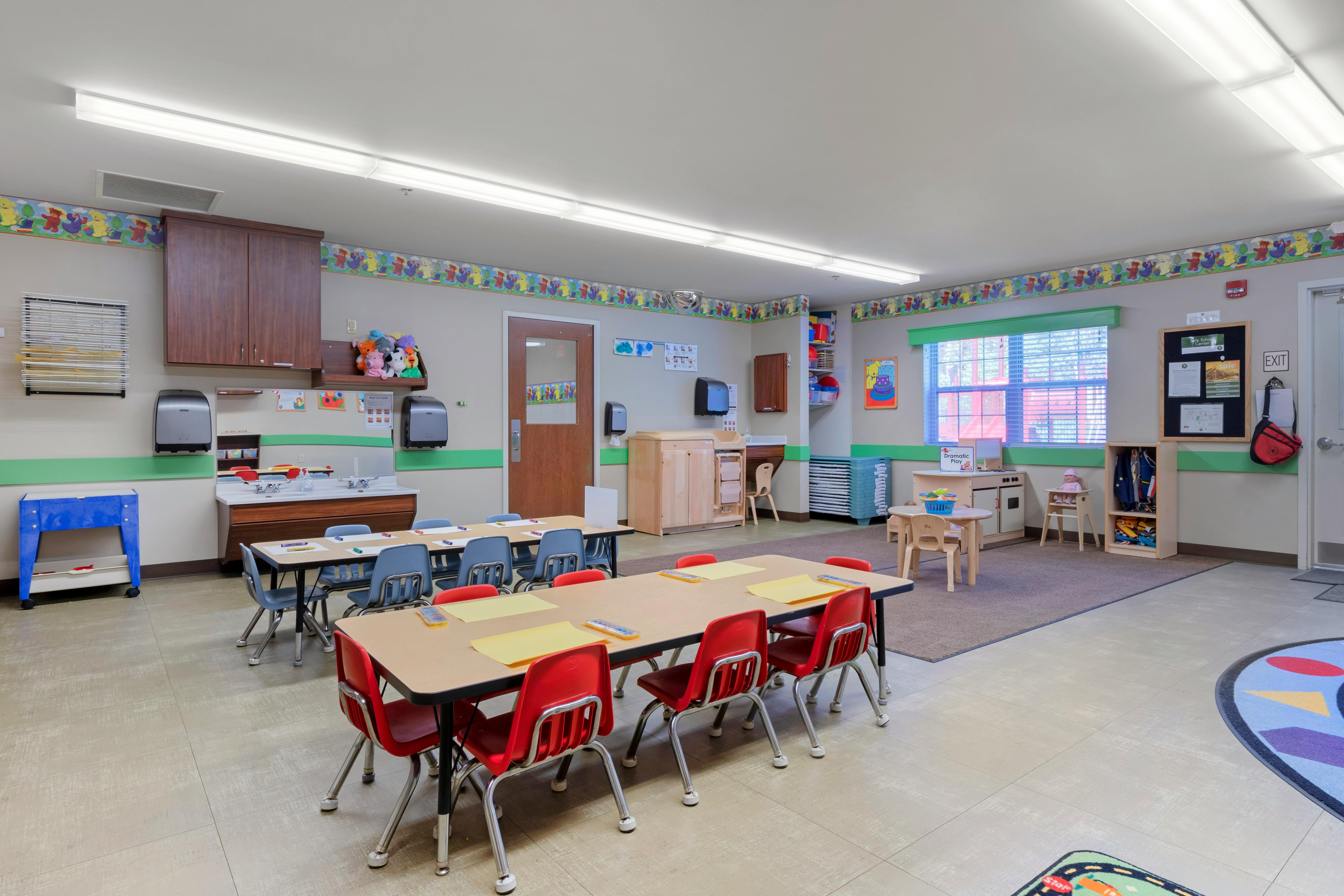 Classroom with child-sized tables and chairs, a sink counter, and play areas