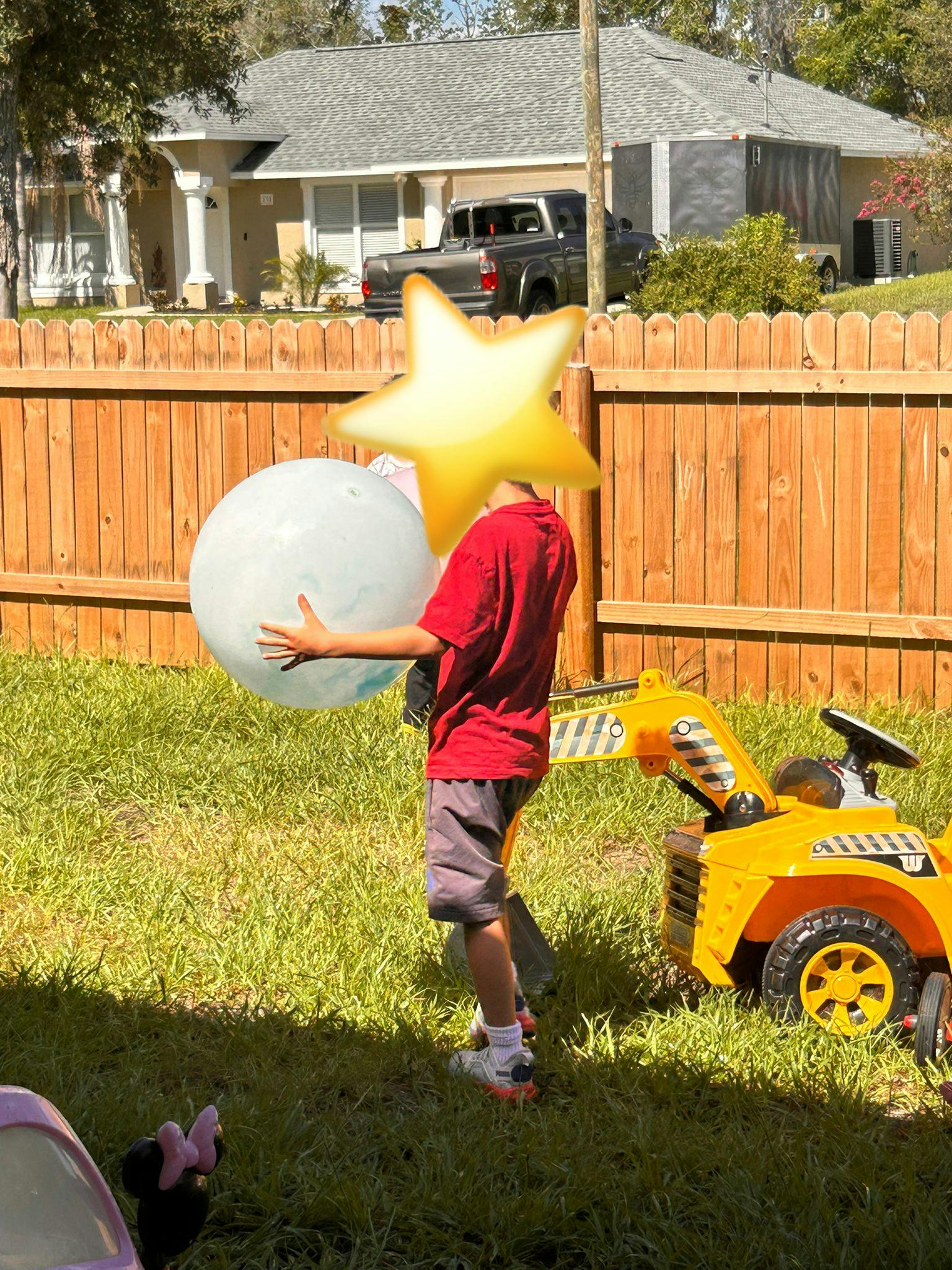 Child holding a large clear ball next to a toy excavator