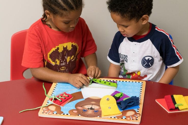 Two children playing with a lacing and buttoning activity board