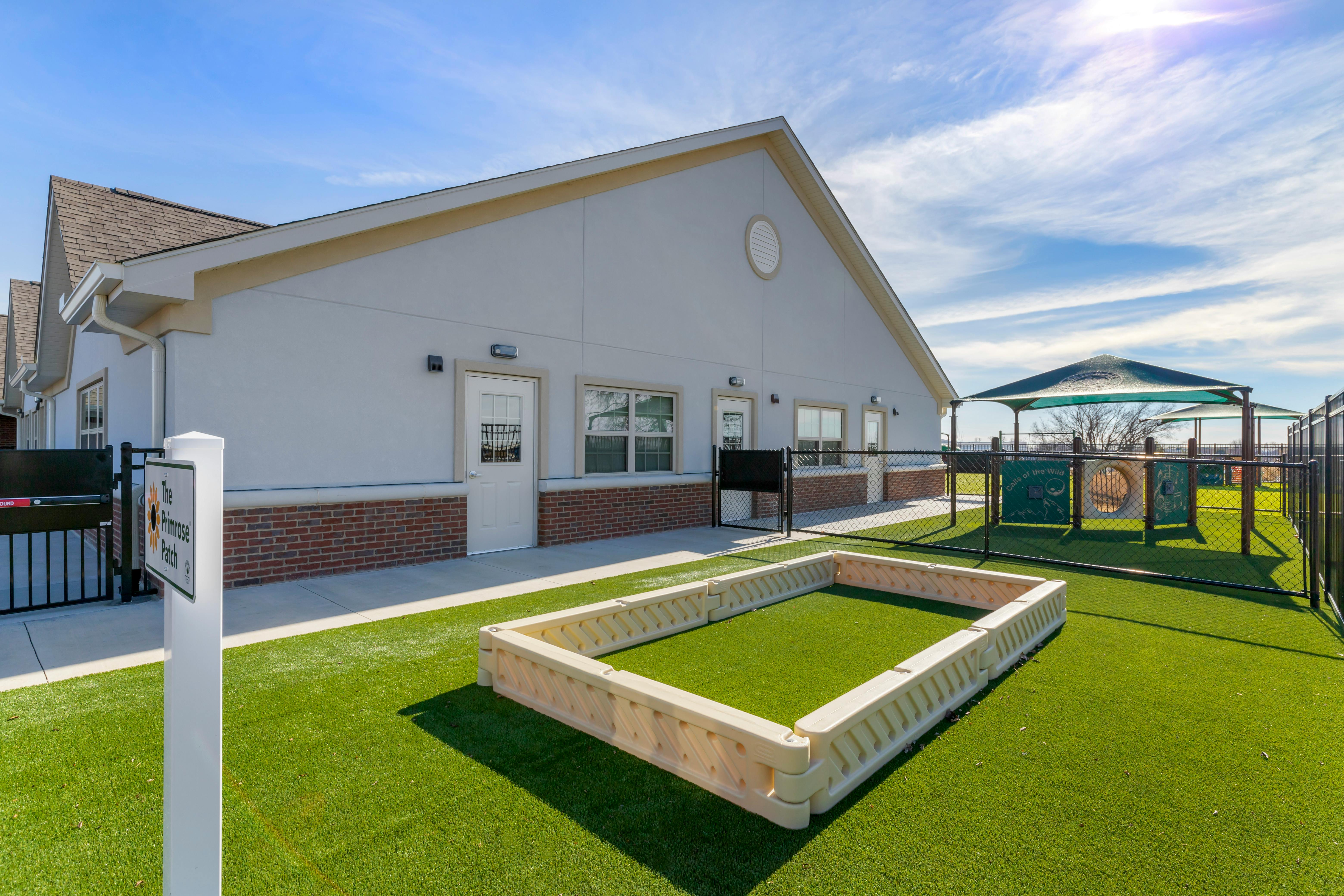 Building with brick base and white upper walls, fenced playground with green turf
