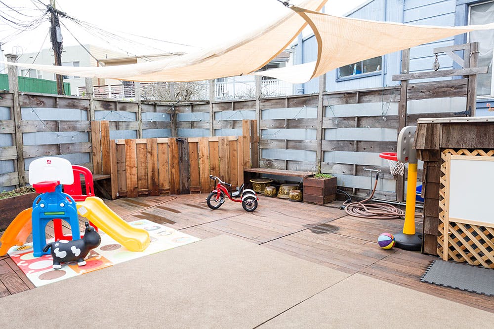 Outdoor play area with slide, tricycle, and basketball hoop under a sunshade