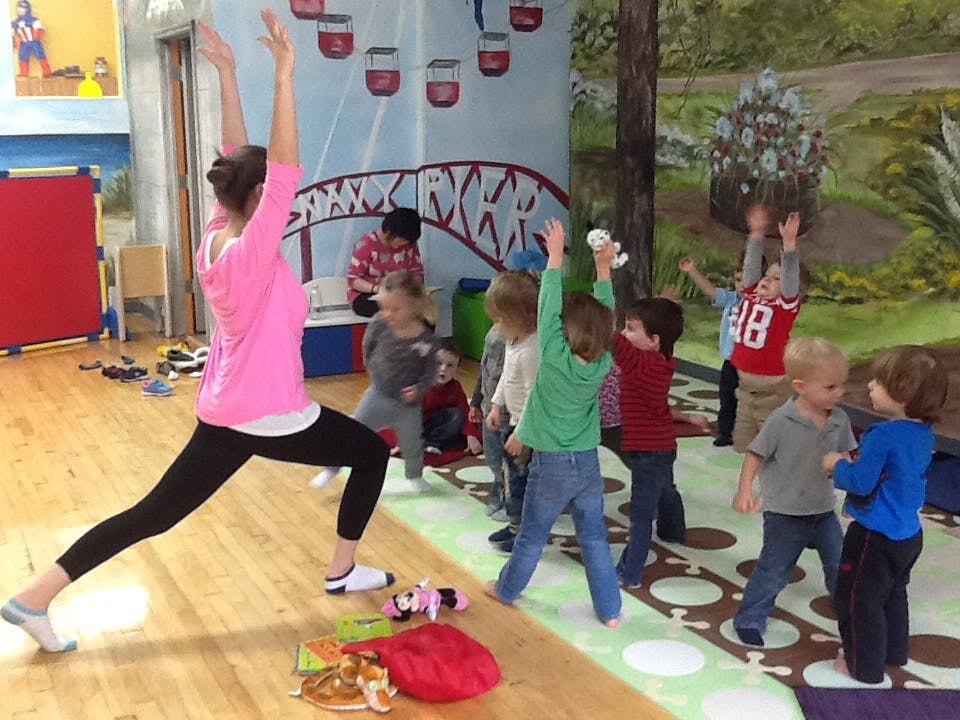 Person leading children in a yoga pose in a classroom