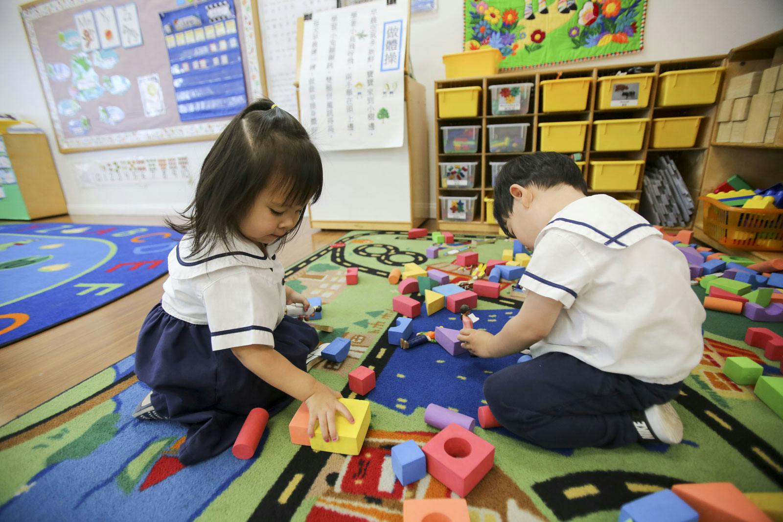Two children playing with blocks on a rug in a classroom